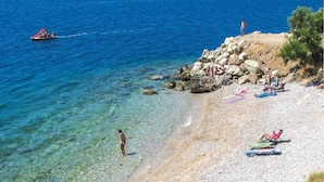 A beach with clear water, a rocky shoreline, and people sunbathing. - Seafront apt with terrace, 4 bedrooms and mooring (Rogoznica)