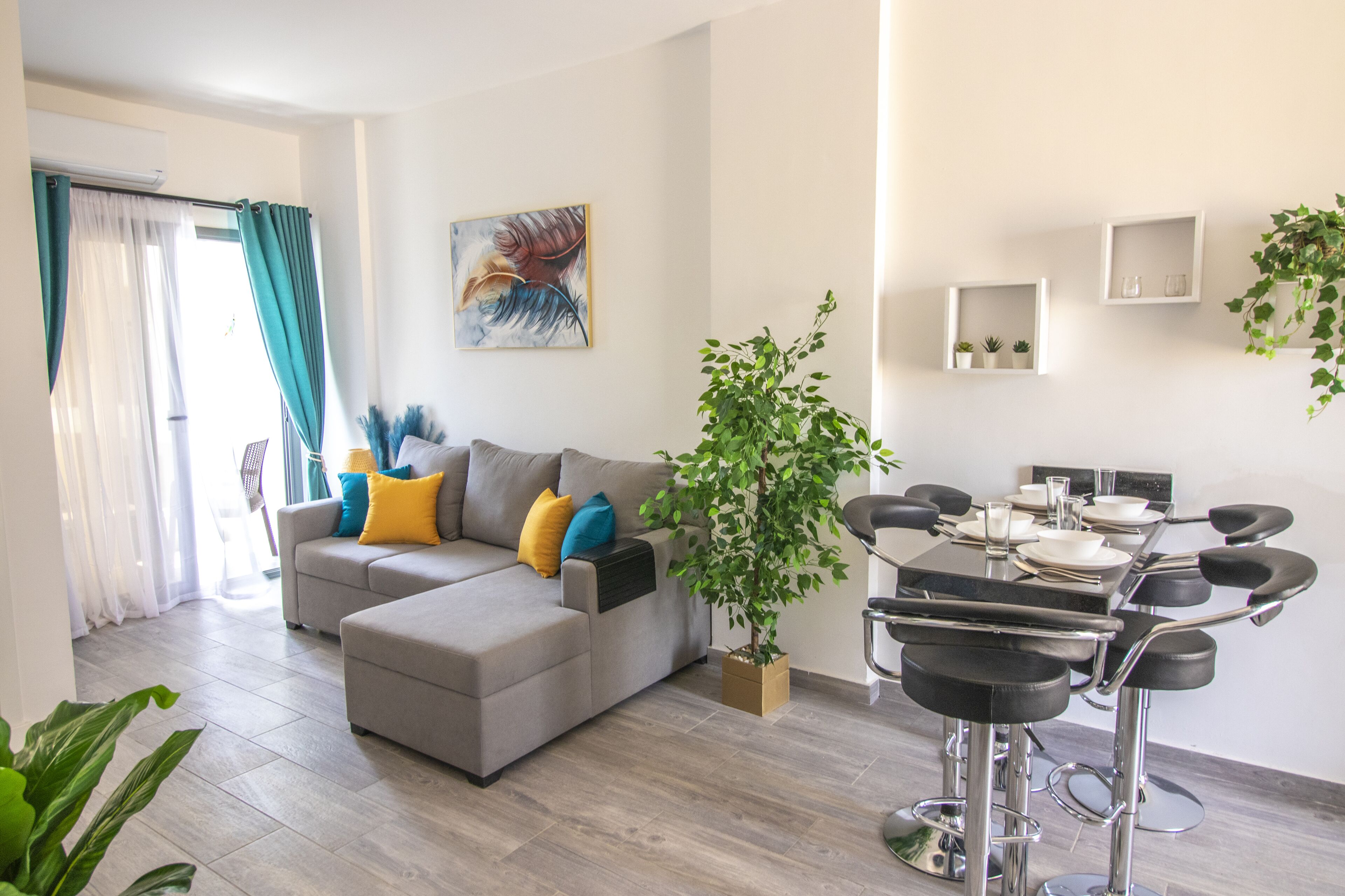 Ein modernes Wohnzimmer mit einem grauen Ecksofa, einem Esstisch mit Barhocker und einer Topfpflanze.