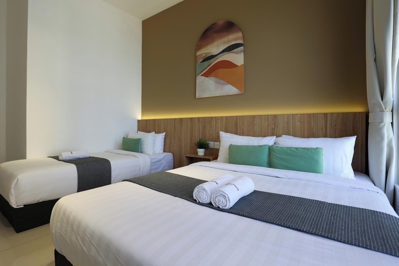A hotel room with two beds, a wooden headboard, a wall-mounted painting, and a potted plant.