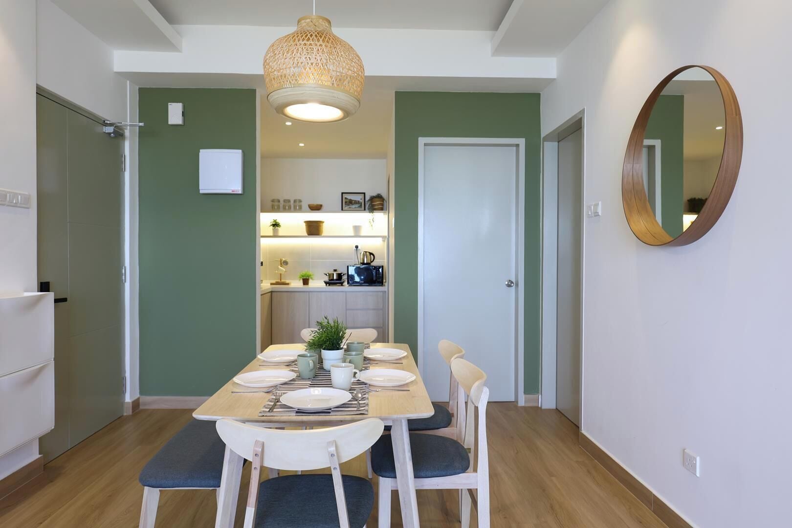 A dining area with a wooden table set for four, surrounded by chairs, a hanging light fixture, and a mirror on the wall.