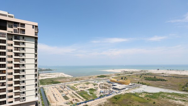 A high-rise building with multiple balconies overlooking a coastal area with sandy beaches and a clear sky. - Bali Deluxe Melaka By I Housing  (Malacca City)