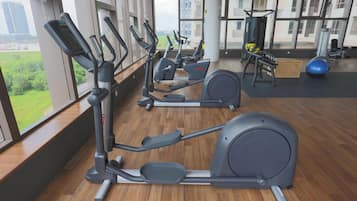 An indoor gym with exercise equipment, large windows, and a view of buildings.