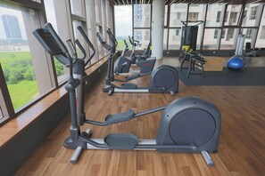 An indoor gym with exercise equipment, large windows, and a view of buildings. - Bali Deluxe Melaka By I Housing  (Malacca City)
