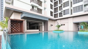 Una piscina con superficie de agua azul cristalina, rodeada por un edificio con varios balcones y una entrada cubierta.