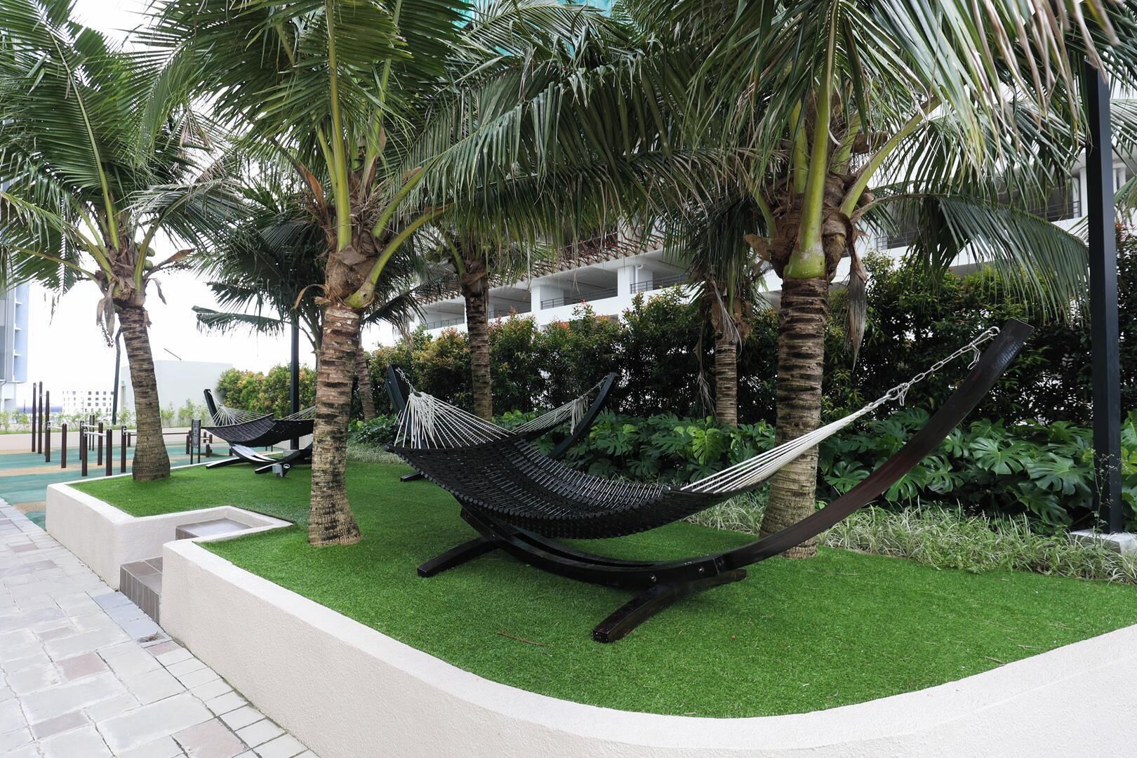 A hammock in a landscaped area with palm trees and a building in the background.