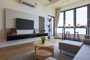 A modern living room with a flat-screen TV, a round wooden table, a sofa, and a balcony with plants. - Bali Deluxe Melaka By I Housing  (Malacca City)