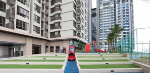 A modern building with multiple floors, a playground area with a red slide, and a pool with artificial grass. - Bali Deluxe Melaka By I Housing  (Malacca City)