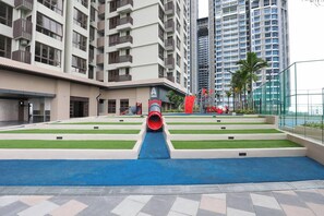 A children's play area with a slide and artificial grass, surrounded by high-rise buildings. - Bali Deluxe Melaka By I Housing  (Malacca City)