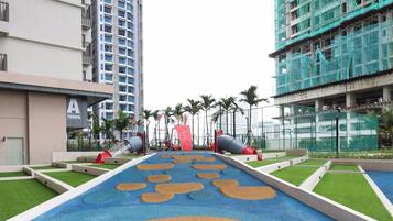 A playground area with slides and artificial grass, surrounded by modern buildings.