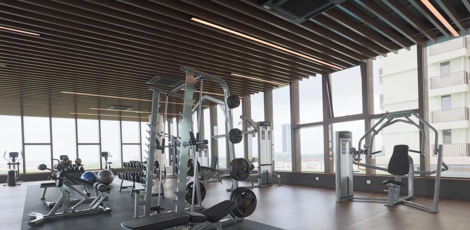 A gym with various exercise equipment, large windows, and a view of buildings.