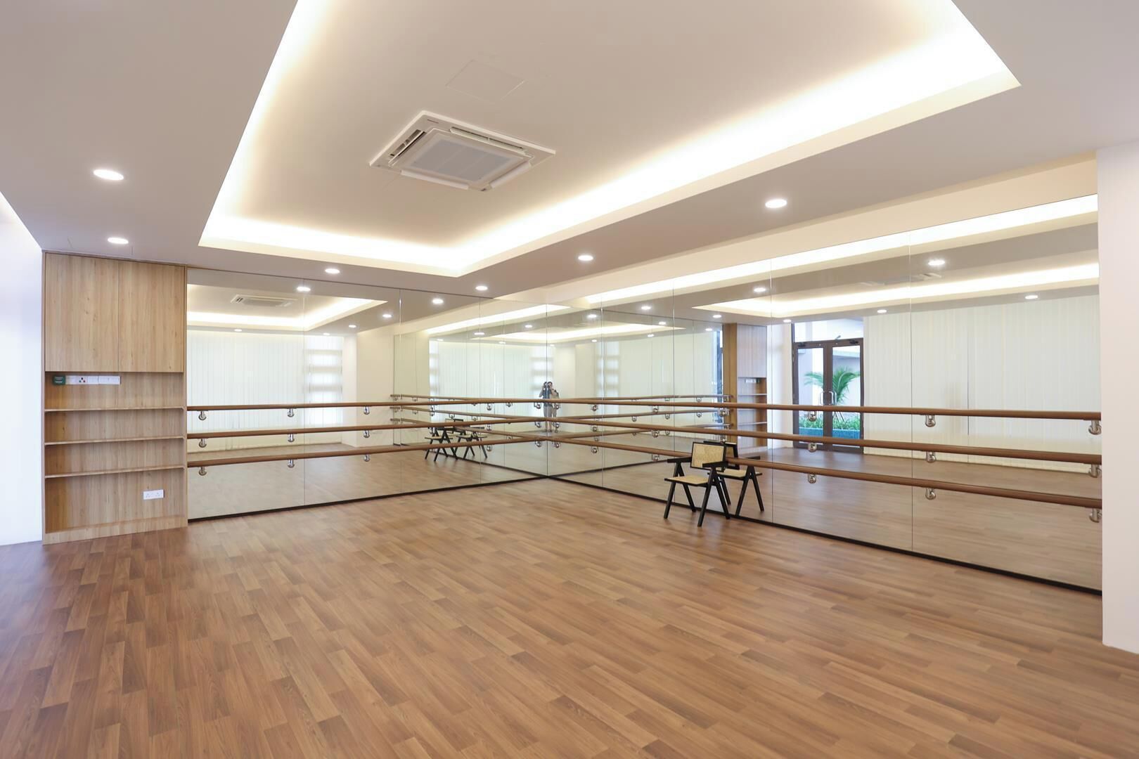 A spacious dance studio with wooden floors, mirrored walls, and a ballet barre.