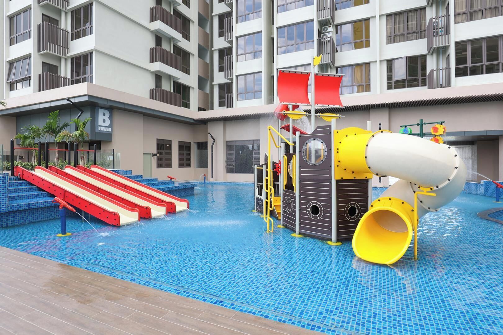 Una piscina interior con tobogán, zona de juegos acuáticos y un edificio con balcones al fondo.