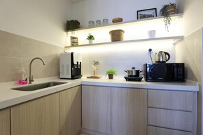 A modern kitchen with a built-in sink, a coffee machine, a microwave, and a shelf with decorative items.