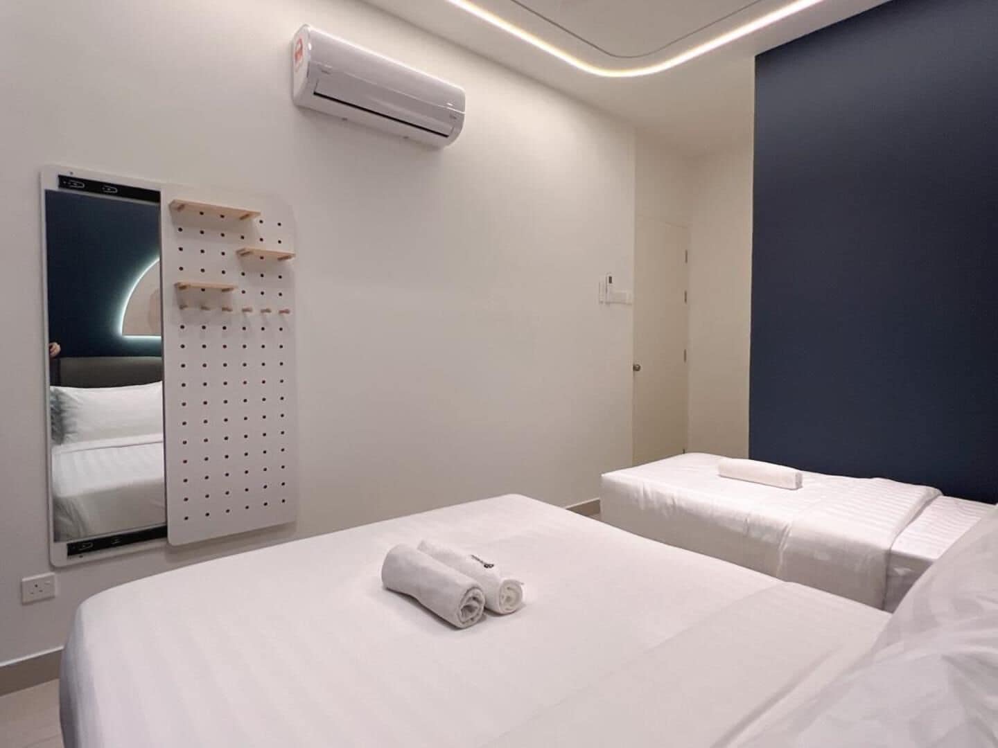 Habitación de hotel con cama, aire acondicionado de pared, espejo y armario con tablero perforado.