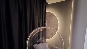 Una habitación moderna con una silla colgante, una lámpara circular grande y una cortina negra.