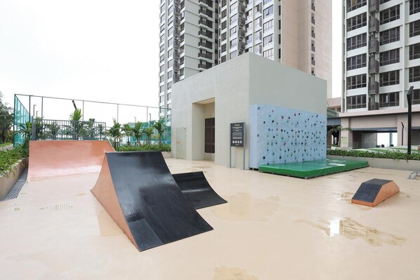 An outdoor recreational area with a climbing wall, a ramp, and a small building, surrounded by high-rise residential buildings.