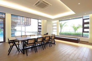 A spacious room with a large dining table and chairs, large windows with a view of a pool and greenery, and a built-in bench along the windows. - Bali Deluxe Melaka By I Housing  (Malacca City)