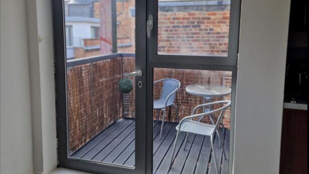 Un balcon avec une chaise en métal et une petite table ronde, un mur en briques et une rambarde en métal.