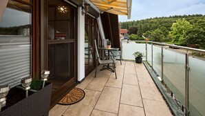 Un balcon avec une table et des chaises, un pot de fleurs et une vue sur une zone boisée.