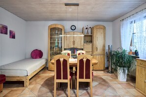 A compact living space with a bed, dining table, chairs, wooden cabinets, a clock, and a potted plant.