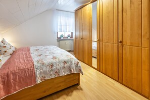 A bedroom with a wooden bed, a wardrobe, a window with curtains, and a radiator.