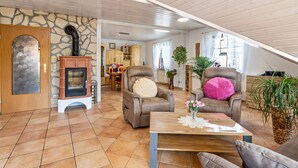 Un salon avec un mur en pierre, une cheminée, deux fauteuils, une table basse et, au fond, un coin repas.