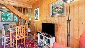 Ein Holzinnenraum mit Treppe, einem Esstisch mit Stühlen, einem Fernseher auf einem Schrank und gerahmten Bildern an den Wänden.