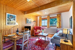 En inredning med träpanel, ett matbord, stolar, en soffa, en röd fåtölj, ett litet bord med en vas och ett element.
