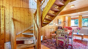 Ein Holzinnenraum mit Treppe, einem Essbereich mit Stühlen und Tisch sowie einem Wohnzimmer mit Sofa und Couchtisch.