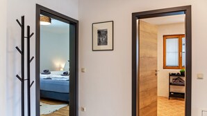 Un pasillo con un espejo, un cuadro enmarcado y una puerta de madera que da a un baño con toallero y ventana.
