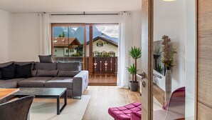Una sala de estar moderna con un sofá, una mesa de centro y un sillón rosa. Hay un ventanal con vistas a casas y montañas.