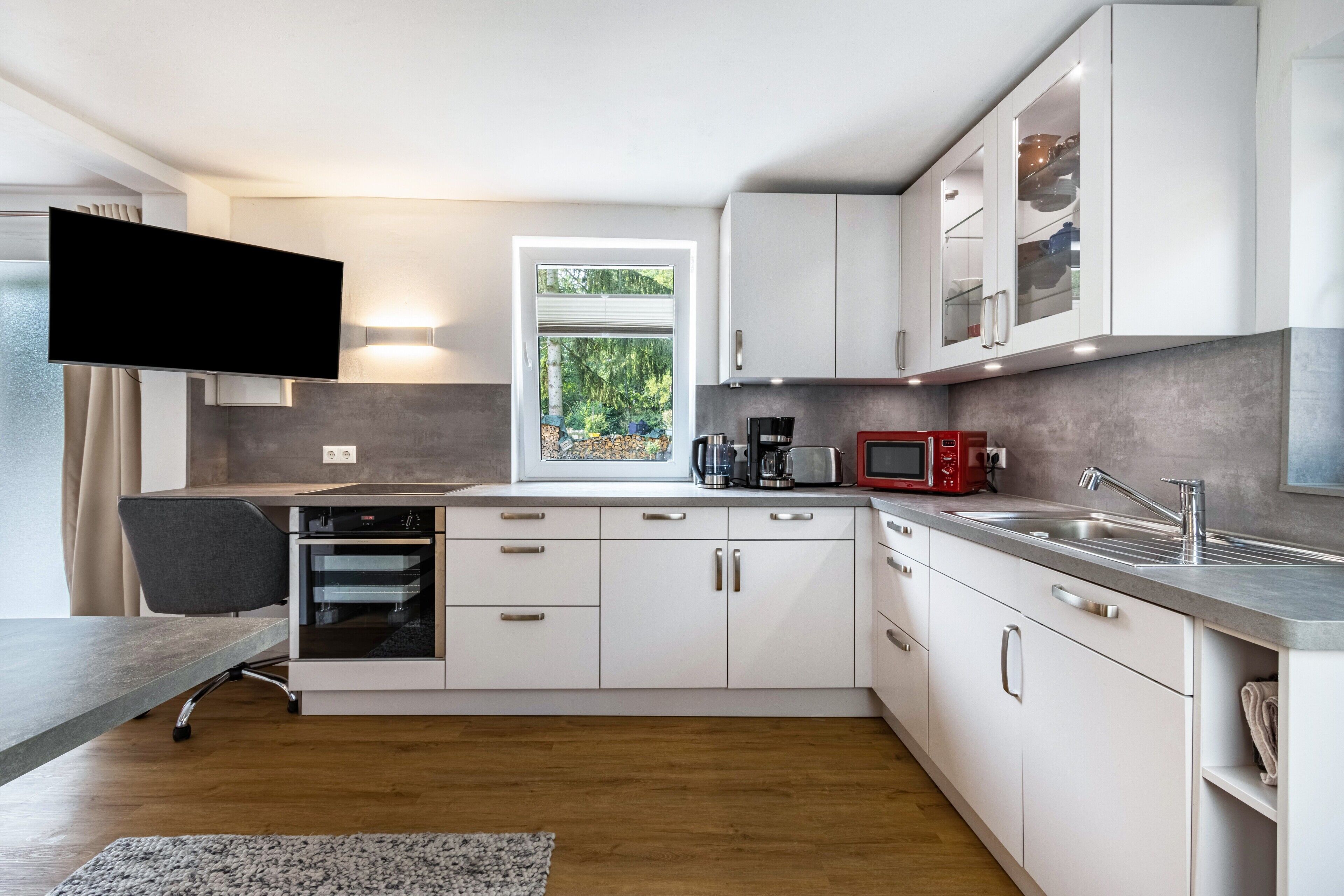 Eine moderne Küche mit weißen Schränken, einem eingebauten Backofen, einer Mikrowelle und einem Spülbecken.
