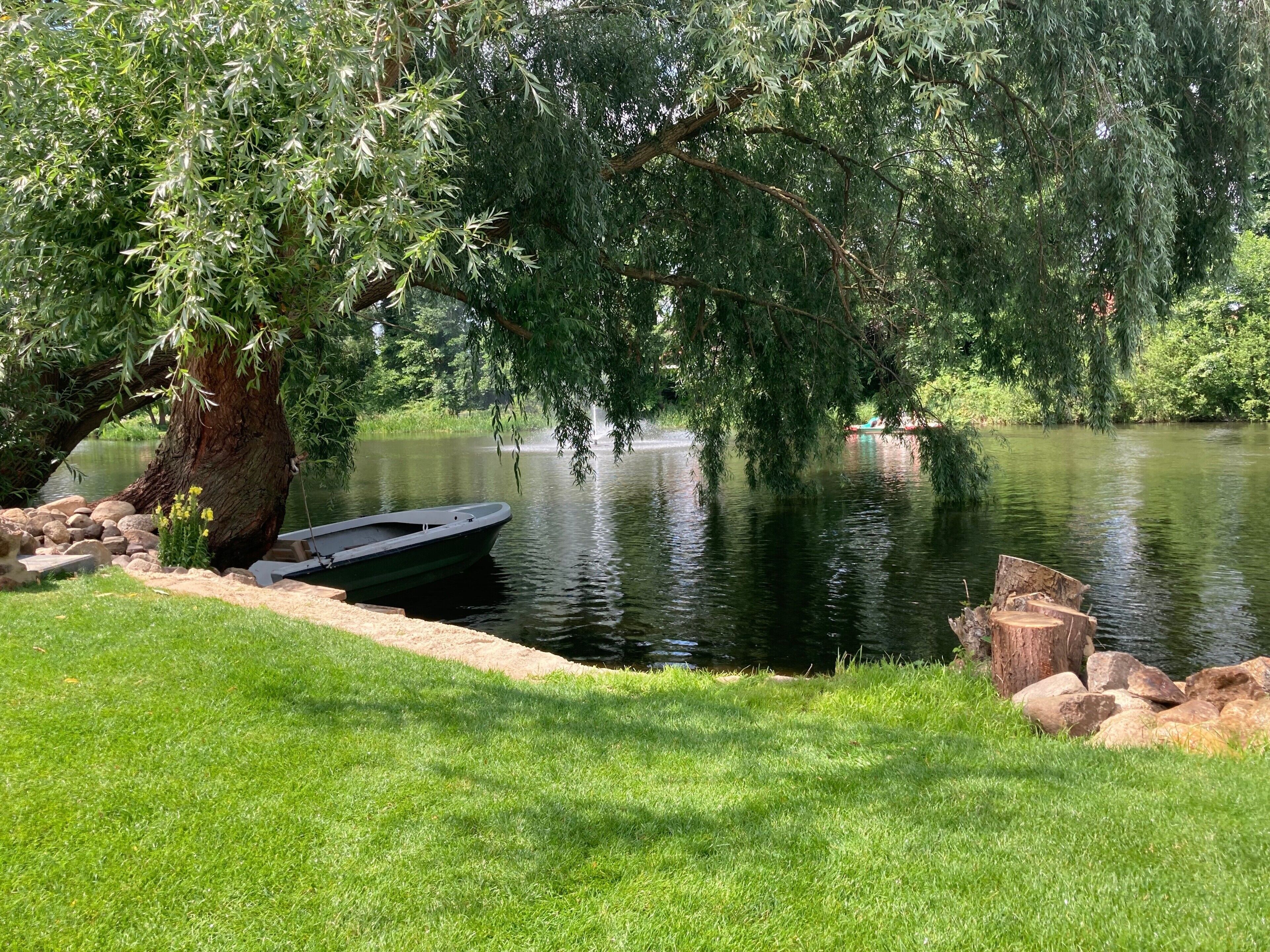 Ein Boot liegt an einem ruhigen Fluss, umgeben von üppigem Grün und einem großen Baum.