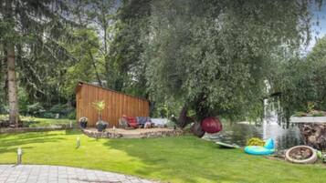 Un cobertizo de madera, un estanque con una fuente y un árbol con una gran esfera roja.