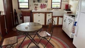 A compact kitchen with a round glass table, two chairs, a stove, a sink, and a refrigerator. - Amazing Secluded cottage under huge trees, on a working Ranch. (Flatonia)