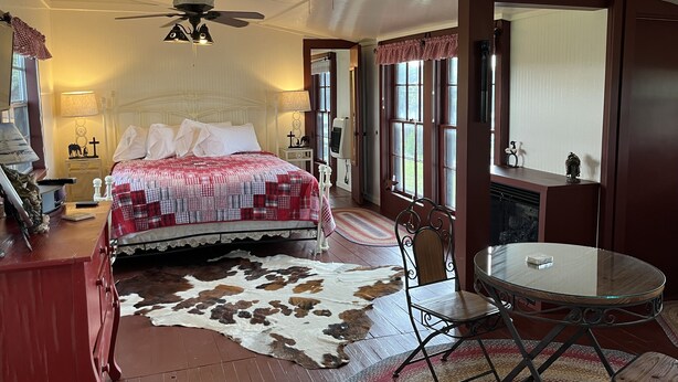 A bedroom with a large bed, a ceiling fan, a round table, and a cowhide rug. - Amazing Secluded cottage under huge trees, on a working Ranch. (Flatonia)