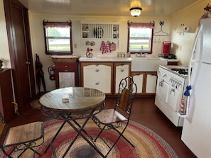 A compact kitchen with a round glass table, wooden chairs, a refrigerator, and a stove. - Amazing Secluded cottage under huge trees, on a working Ranch (Flatonia)