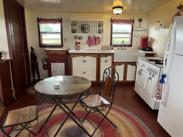 A compact kitchen with a round glass table, wooden chairs, a refrigerator, and a stove. - Amazing Secluded cottage under huge trees, on a working Ranch (Flatonia)