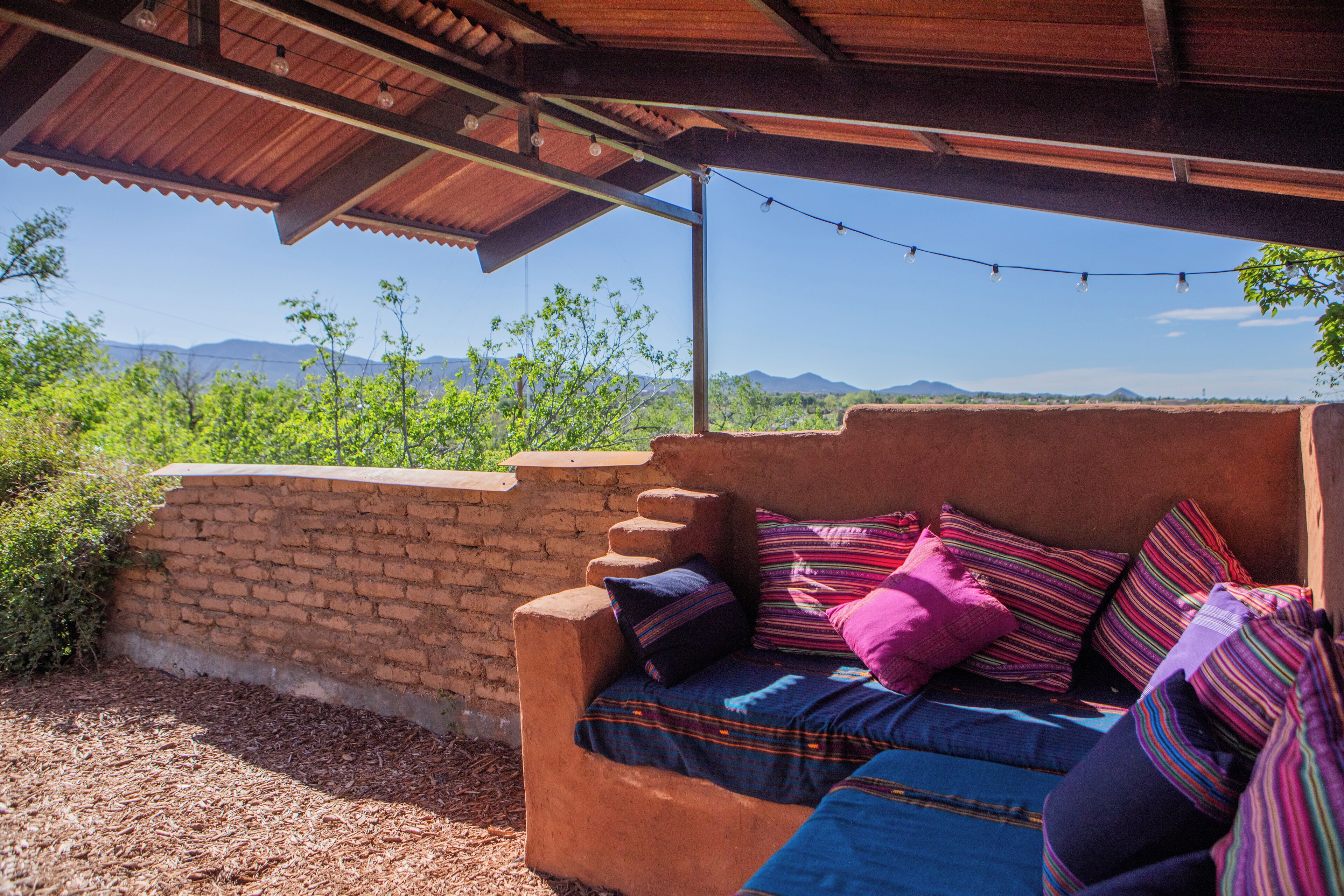 Un espace extérieur aménagé dans un style rustique, avec un mur en briques, un banc en bois et des coussins aux couleurs vives.