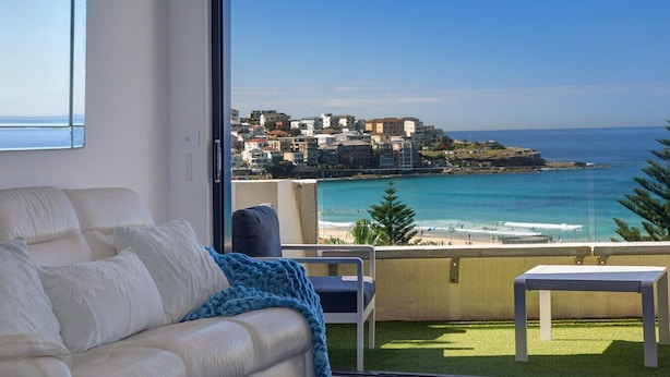 Ein Balkon mit Blick auf das Meer, ein weißes Sofa und ein kleiner Tisch.