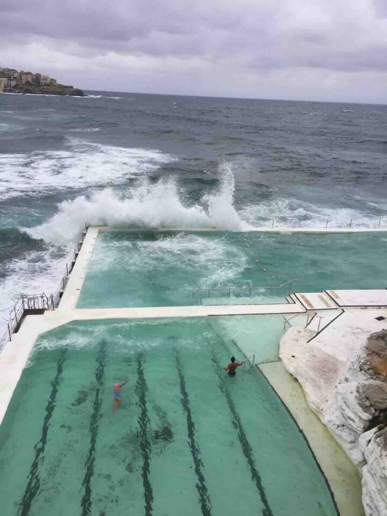 A swimming pool with a view of the ocean and waves crashing onto the shore.