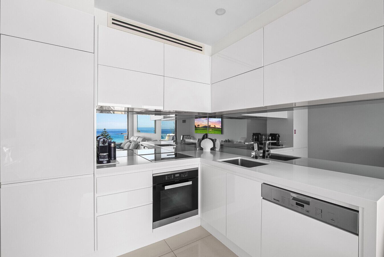 A modern kitchen with a built-in dishwasher, a coffee machine, and a view of the ocean.