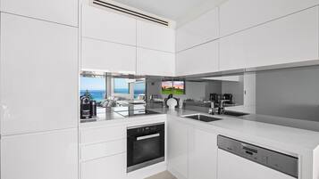 A modern kitchen with a built-in dishwasher, a coffee machine, and a view of the ocean.