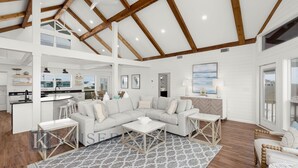 A spacious living area with a large sectional sofa, a dining table, and a kitchen in the background. - Modern Beach Front Home with Private Beach Access | Trillion Dollar View by Kaiser (Gulf Shores)