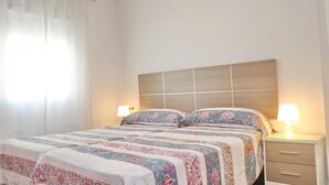 Une chambre à coucher avec un lit, deux tables de chevet, une commode et une fenêtre avec des rideaux.