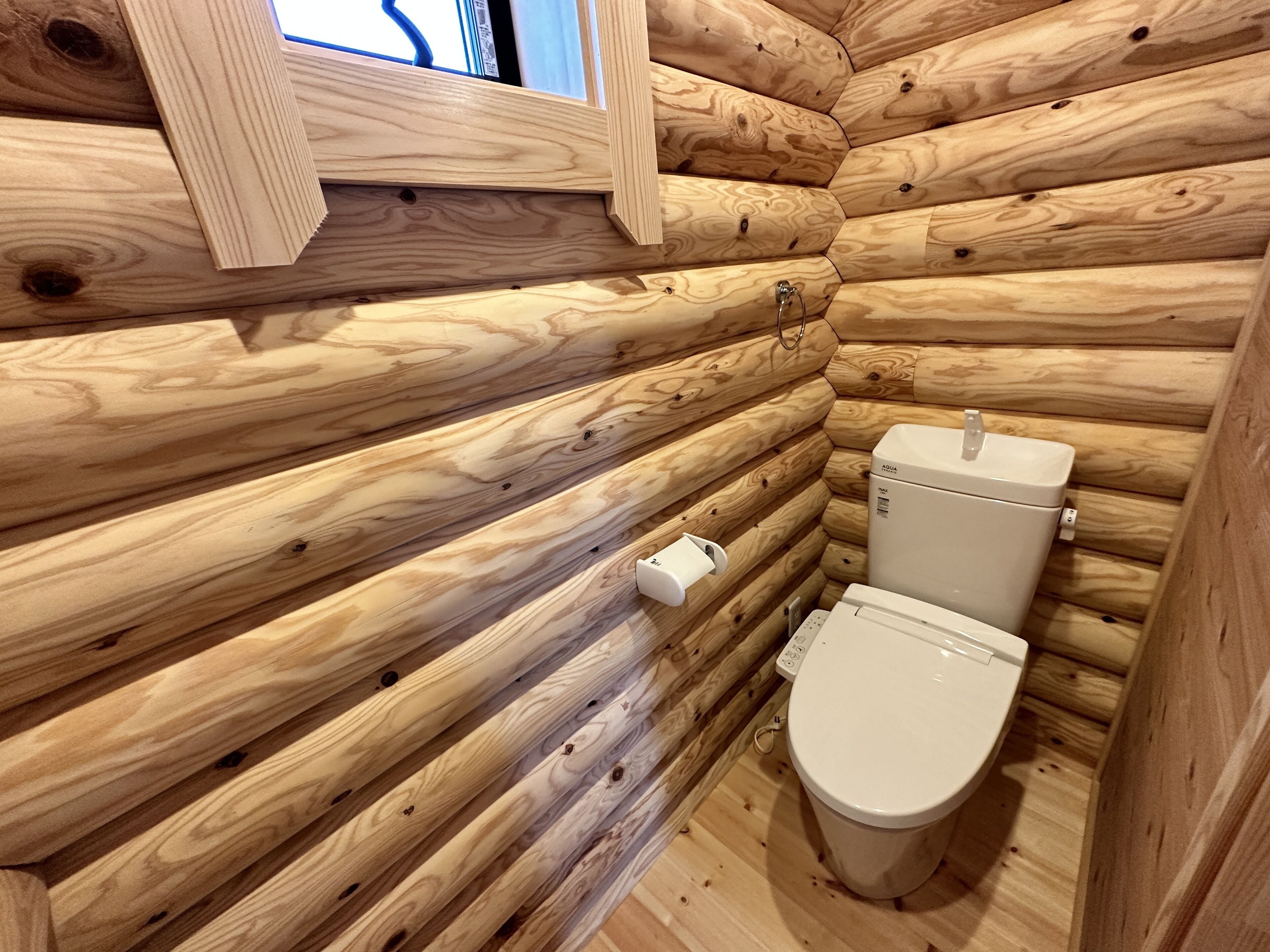 A wooden cabin bathroom with a toilet and a window.