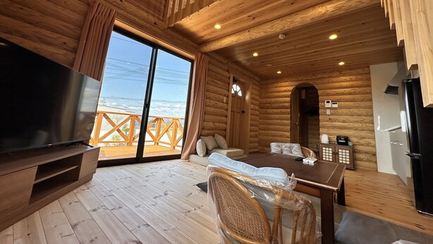 A log cabin interior with a large TV, wooden flooring, a dining area, and a view of the outdoors. - shirahamakashibessoK-32 (Shirahama)