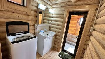 Een compact houten badkamer in een vakantiehuis, met een wasmachine, wastafel en een klein raam.