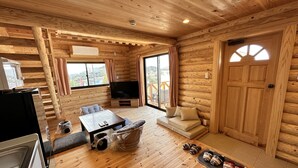 A log cabin interior with a wooden floor, a dining table, a sofa, a TV, and a large window with curtains. - shirahamakashibessoK-32 (Shirahama)