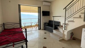 Une pièce comprenant un lit, un canapé, une télévision, un escalier et donnant sur la mer.